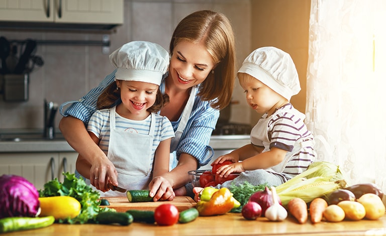 donna e bambini sorridenti con cappello da chef che affettano verdure