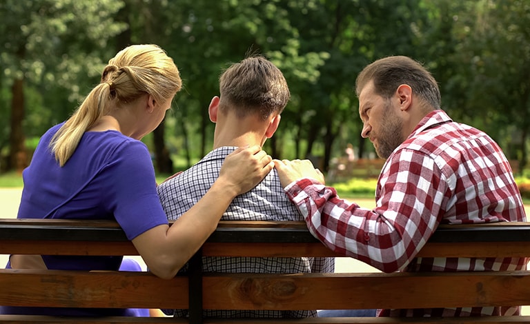genitori a colloquio con il figlio su una panchina in un parco