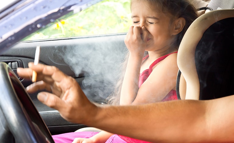adulto che fuma in auto con bimba che si protegge naso e bocca
